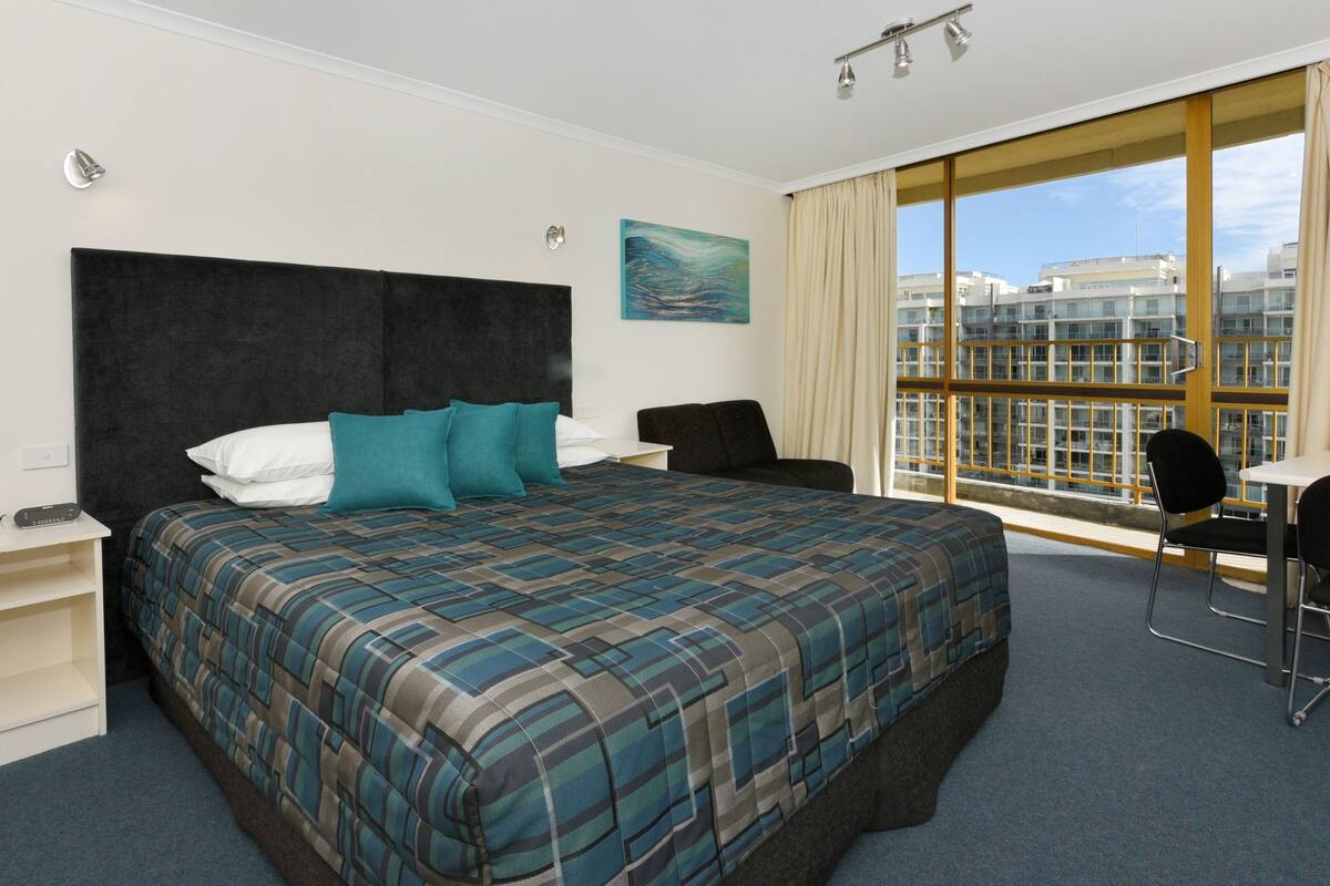 Ett hotellrum med en stor säng, ett skrivbord, en stol och ett fönster med utsikt över staden.