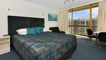 A hotel room with a large bed, a desk, a chair, and a window with a city view.