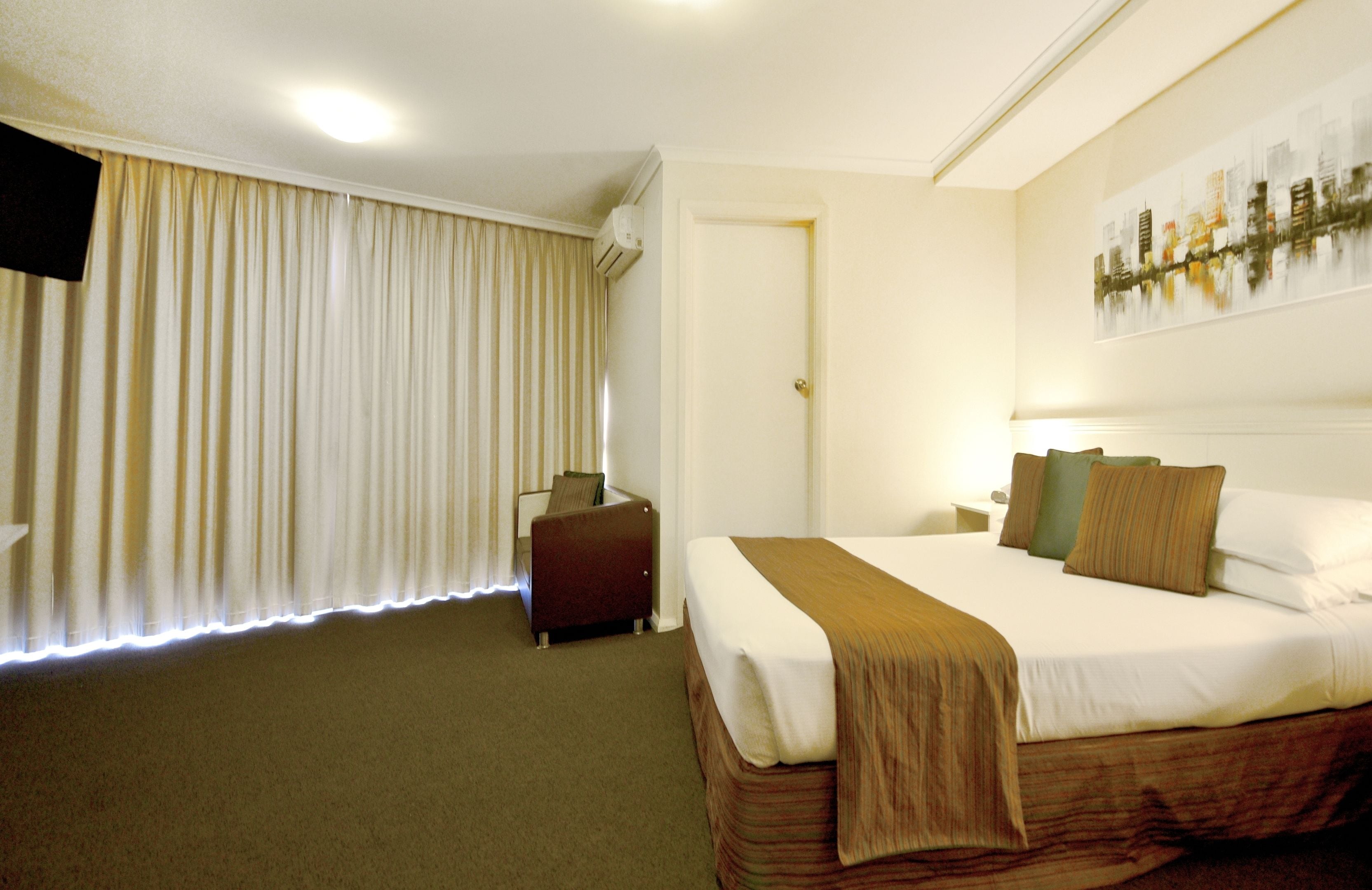 A hotel room with a large bed, a small desk, a chair, and a window with curtains.