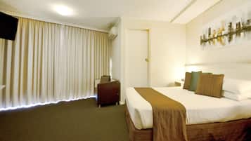 A hotel room with a large bed, a small desk, a chair, and a window with curtains.