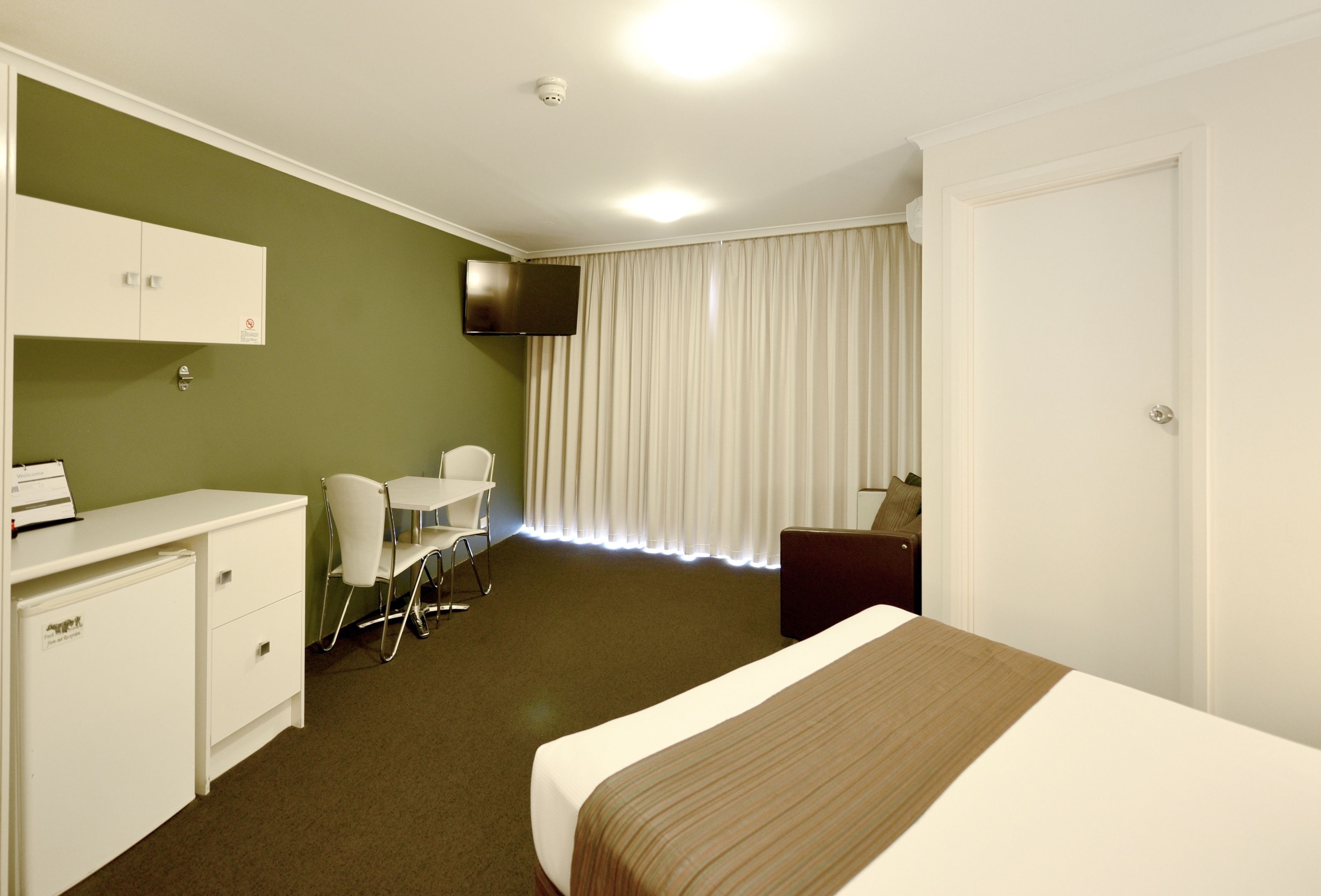 Une chambre d’hôtel comprenant un lit, un bureau avec une chaise, un téléviseur fixé au mur et une porte.