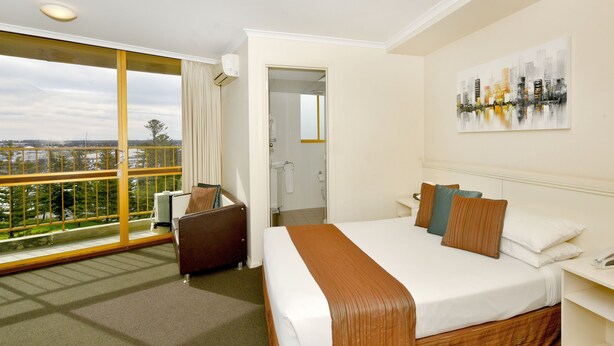 A hotel room with a large bed, a desk, a chair, and a balcony with a city view.