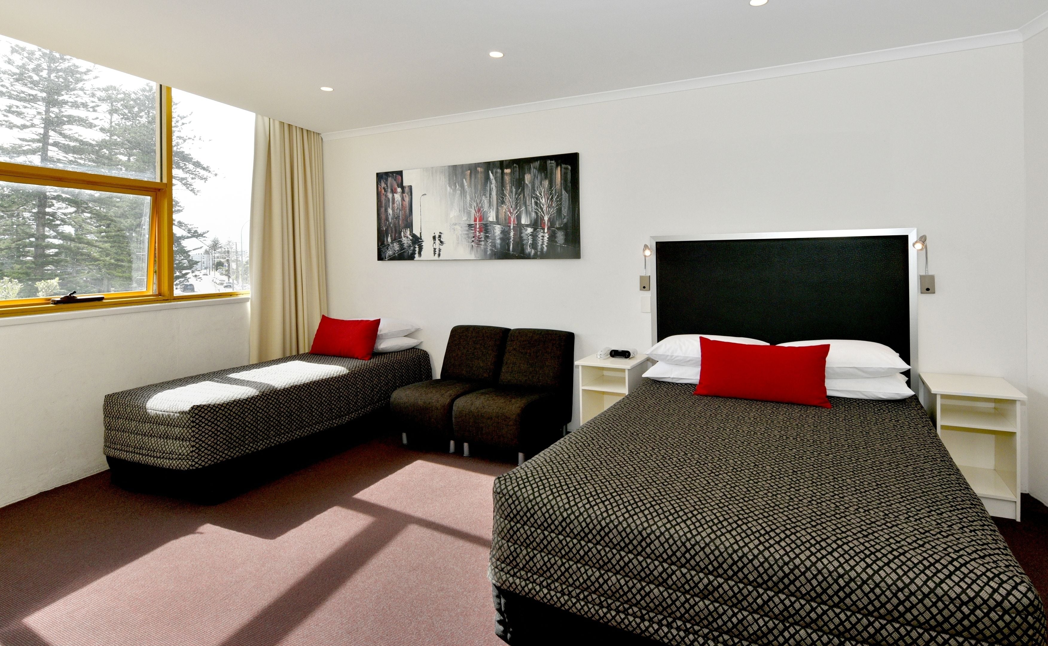 Une chambre d’hôtel avec deux lits simples, un canapé, un tableau au mur et une fenêtre avec des rideaux.