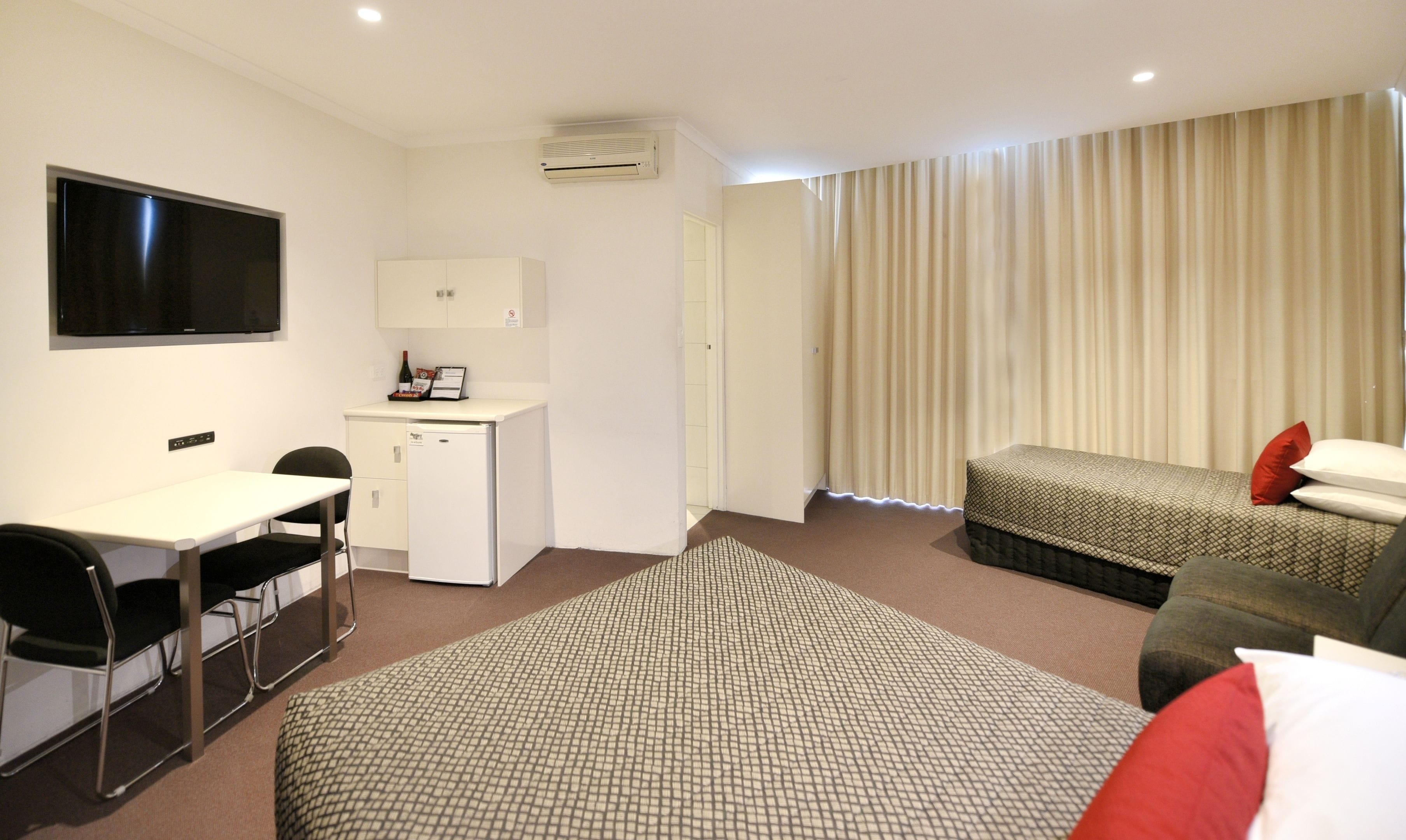 Habitación de hotel con escritorio, un refrigerador pequeño, una cama con ropa de cama estampada y un televisor montado en la pared.