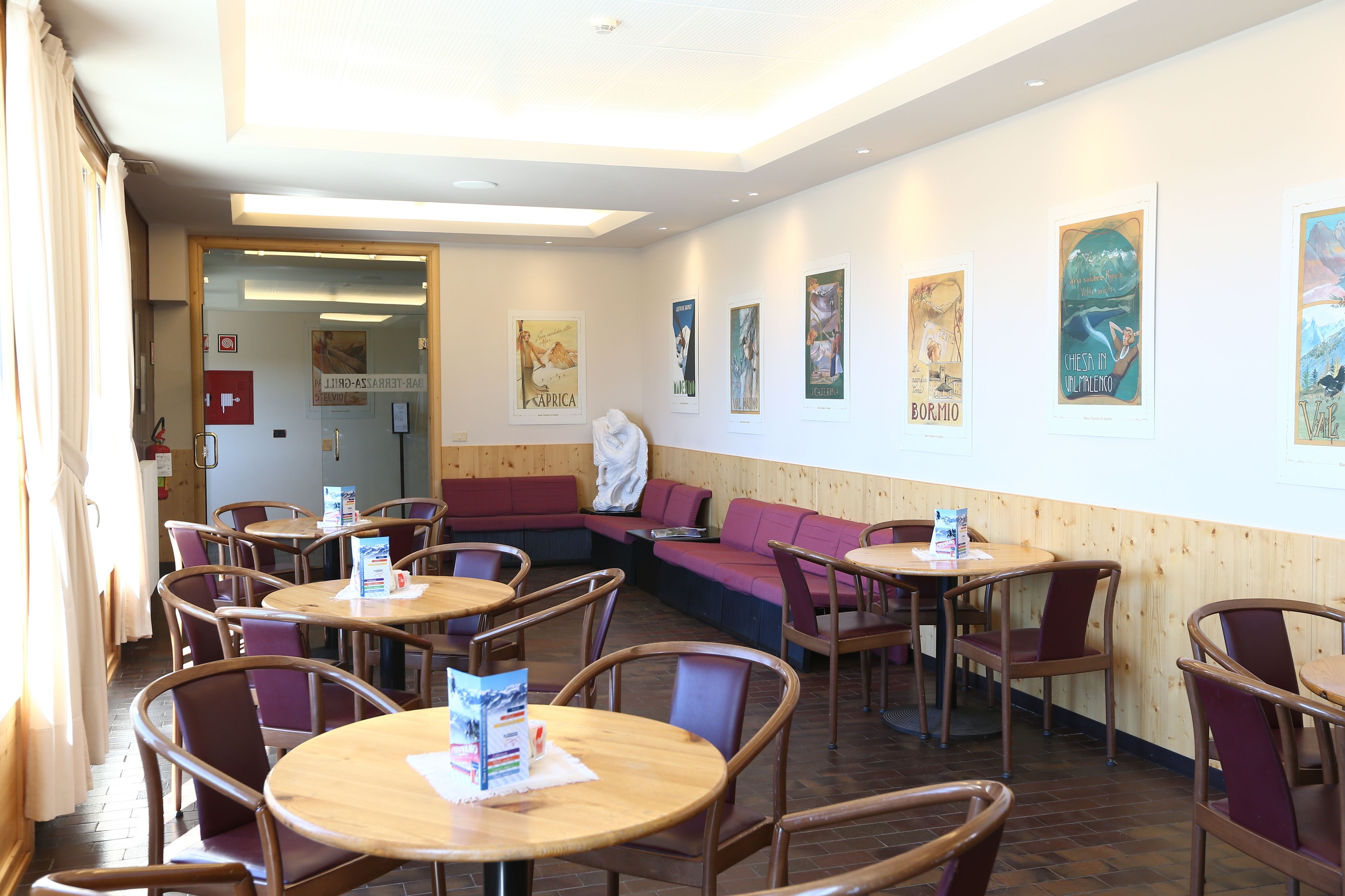 Un restaurante con mesas y sillas de madera, una zona de asientos con bancos rojos y obras de arte en las paredes.
