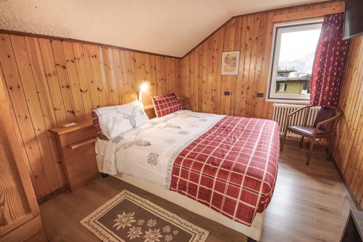 Ein Schlafzimmer mit Holzwänden, einem Bett, einem Nachttisch, einem Stuhl und einem Fenster mit Blick.
