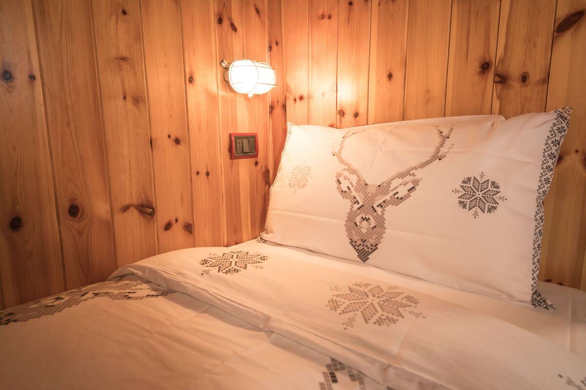 Ein Zimmer mit Holzwänden und einem Bett mit bestickten Kissen.
