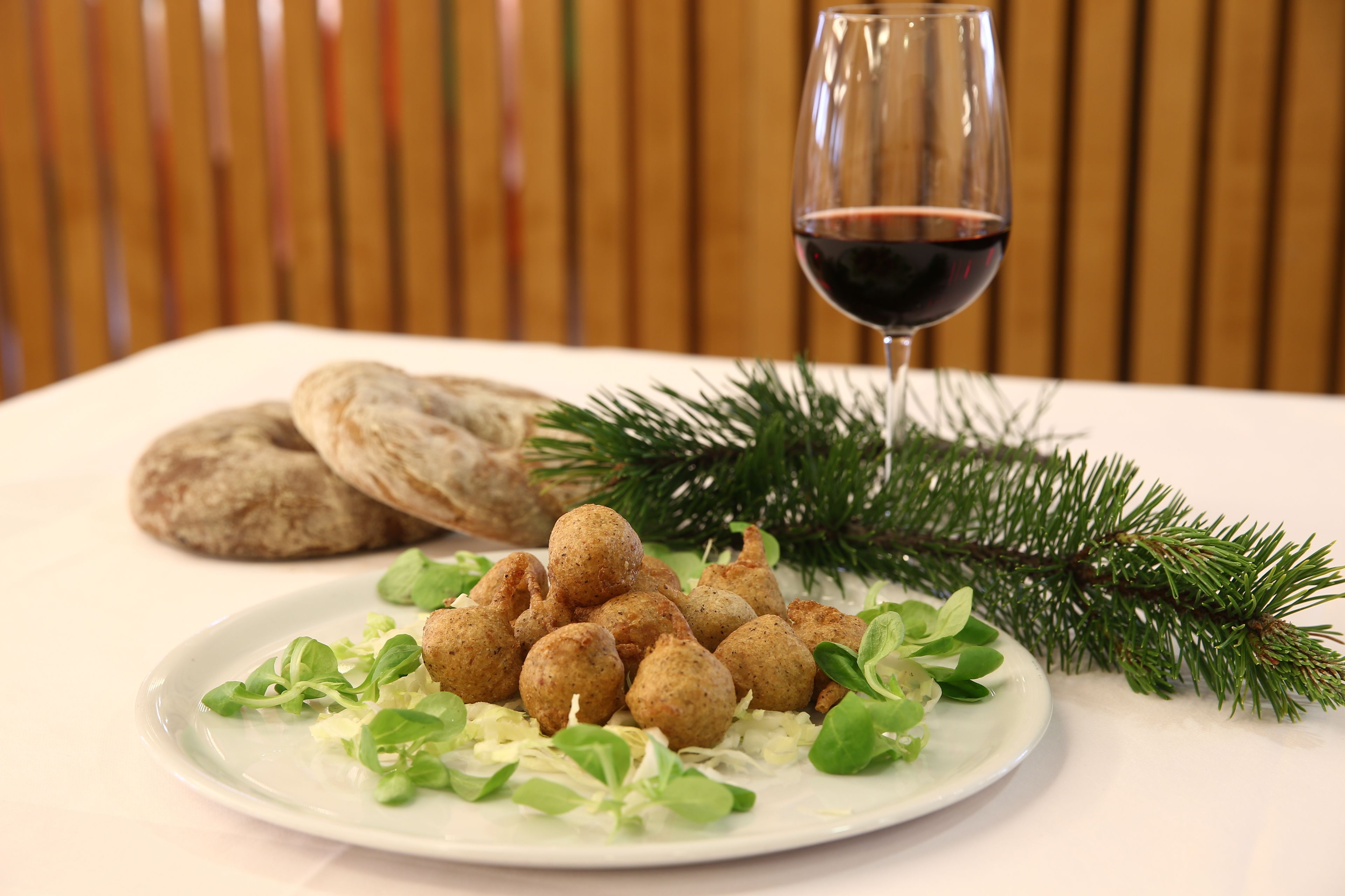 Un plato de comida con pan y una copa de vino tinto sobre una mesa con fondo de madera.