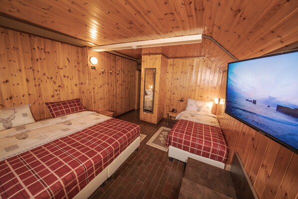 Una habitación tipo cabaña de madera con dos camas, un televisor y un espejo.