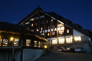A multi-story building with illuminated windows and a sign that reads "PIRAMID." - Albergo Quarto Pirovano (Bormio)