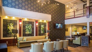 A lobby with a sofa, armchairs, a TV, and artwork on the walls. - Parke Regency Hotel & Conf Ctr (Bloomington)