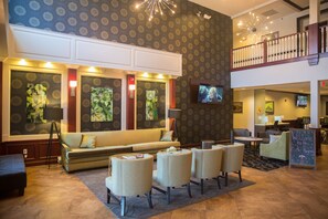 A lobby with a sofa, armchairs, a TV, and artwork on the walls. - Parke Regency Hotel & Conf Ctr (Bloomington)