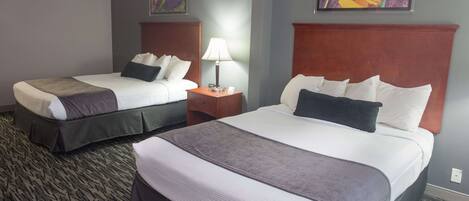 Two beds with headboards, a nightstand with a lamp, and two paintings on the wall.
