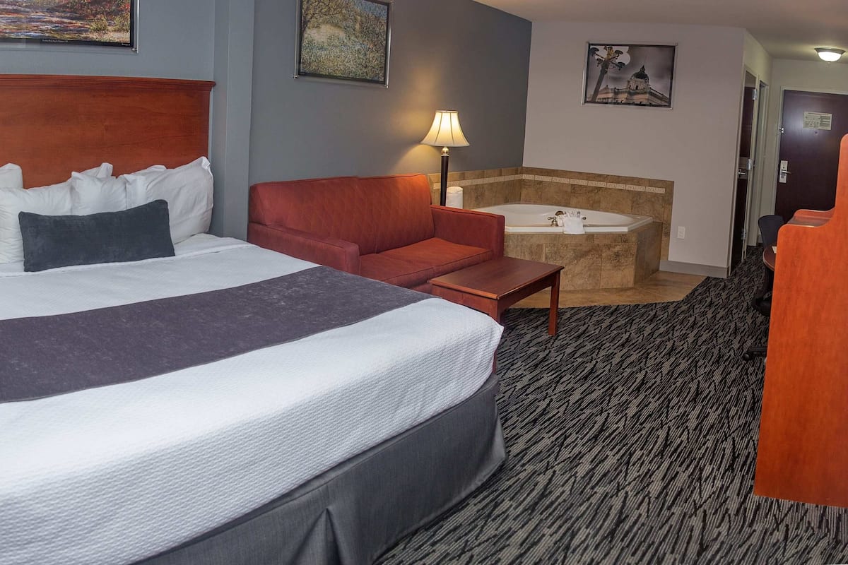 A hotel room with a large bed, a red sofa, a bathtub, and a desk.
