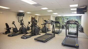 A gym with various cardio machines, a mirrored wall, and a TV mounted on the wall.