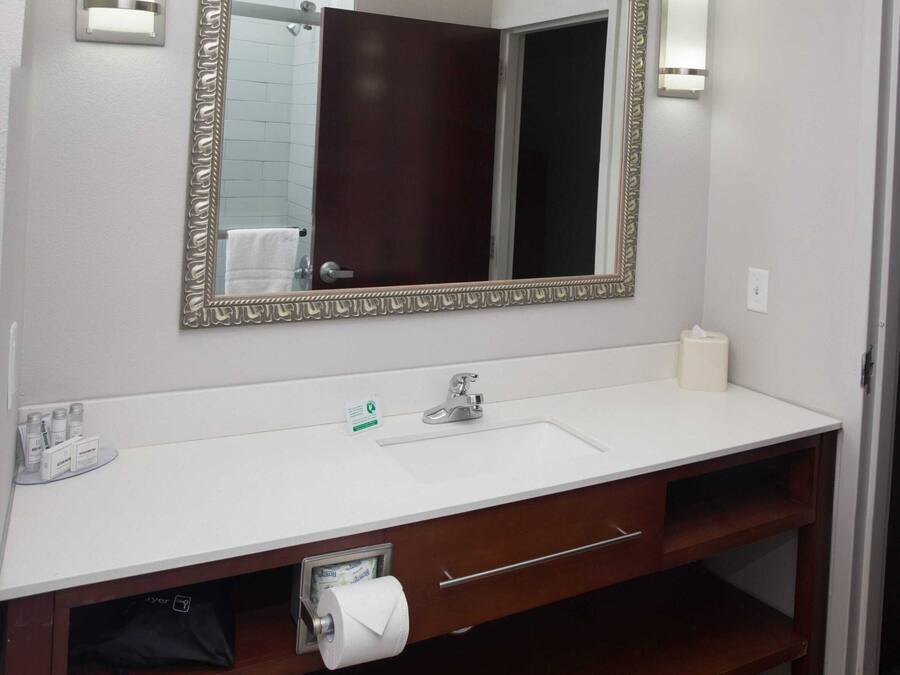 A bathroom with a white sink, a large mirror with a decorative frame, two wall-mounted lights, and a towel rack.