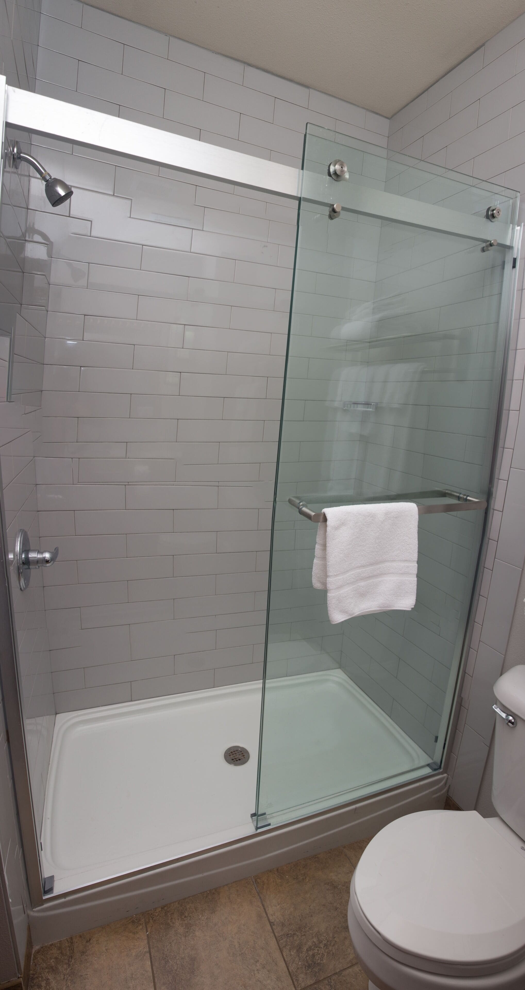 A glass-enclosed shower with a white towel hanging on the door handle, a white toilet, and a tiled wall.