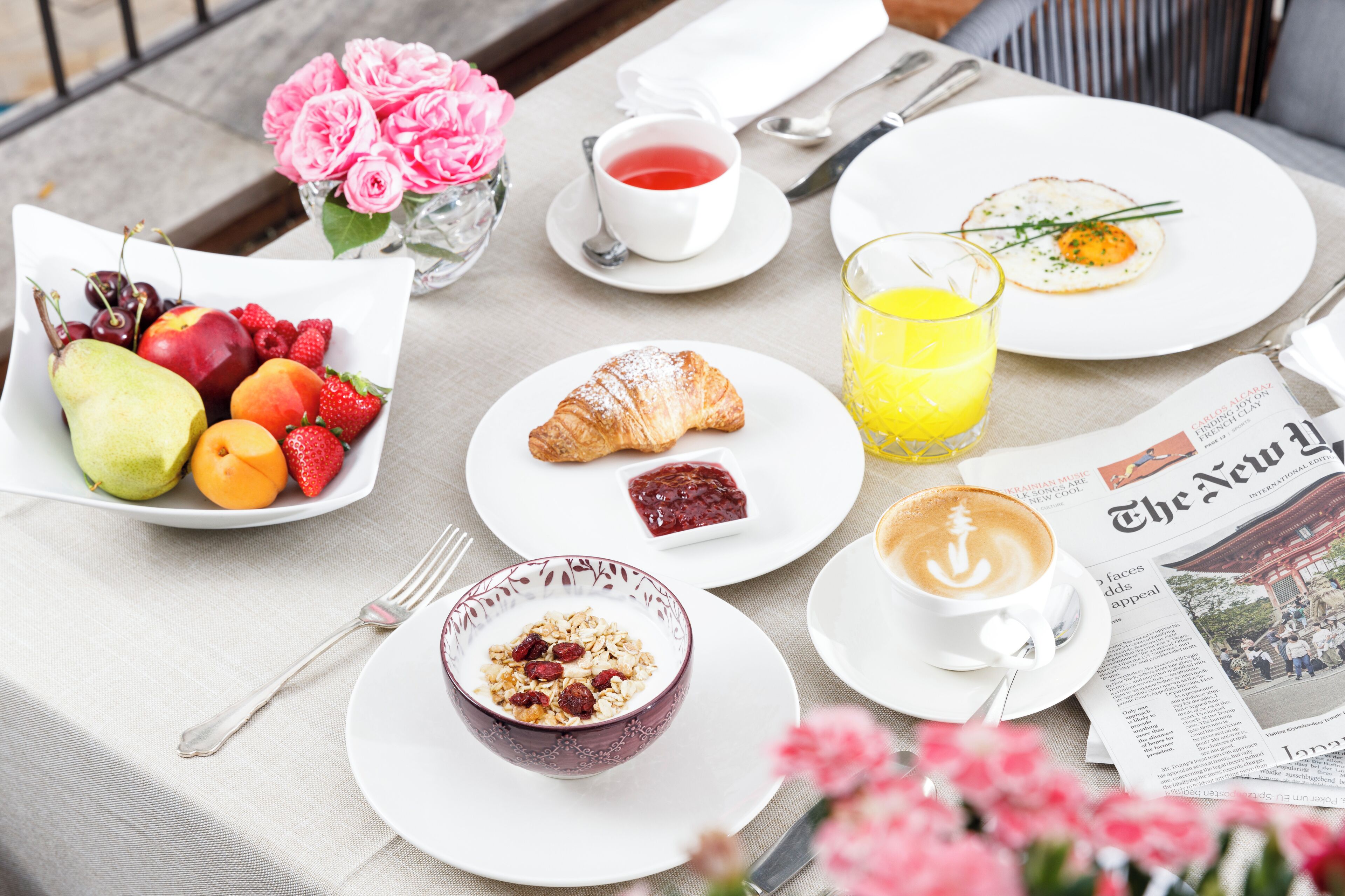 Una mesa de desayuno con un croissant, un frutero, café y un periódico.
