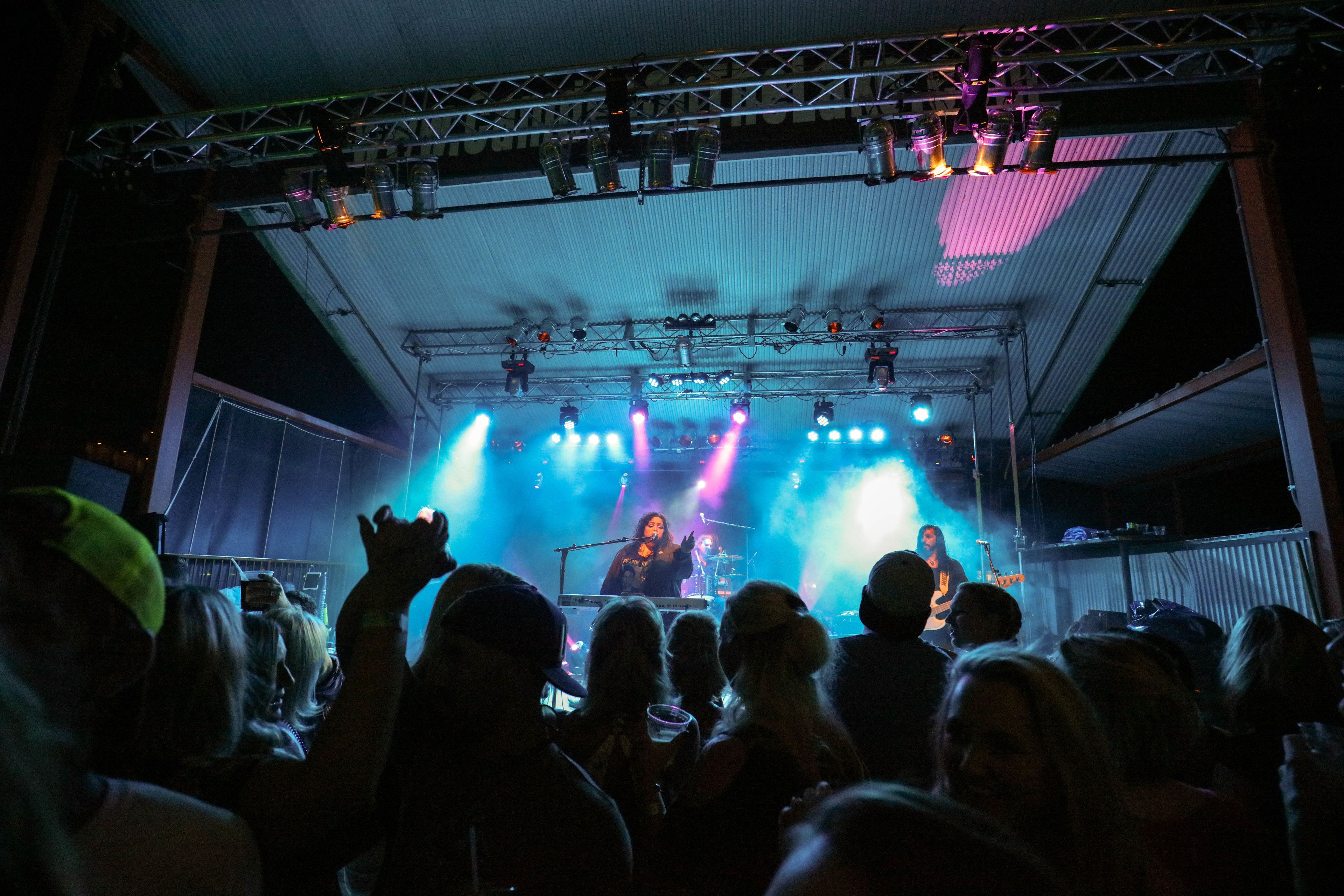 A stage with a band performing, illuminated by stage lights, and an audience in front.