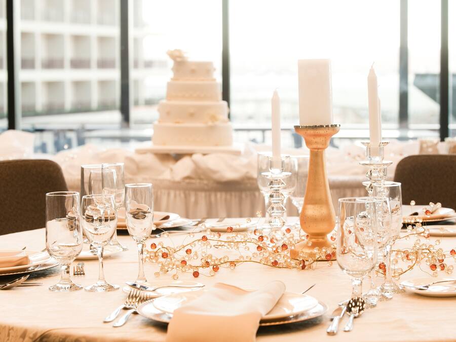 A table set for a formal event with a tiered white cake, candles, and glassware.