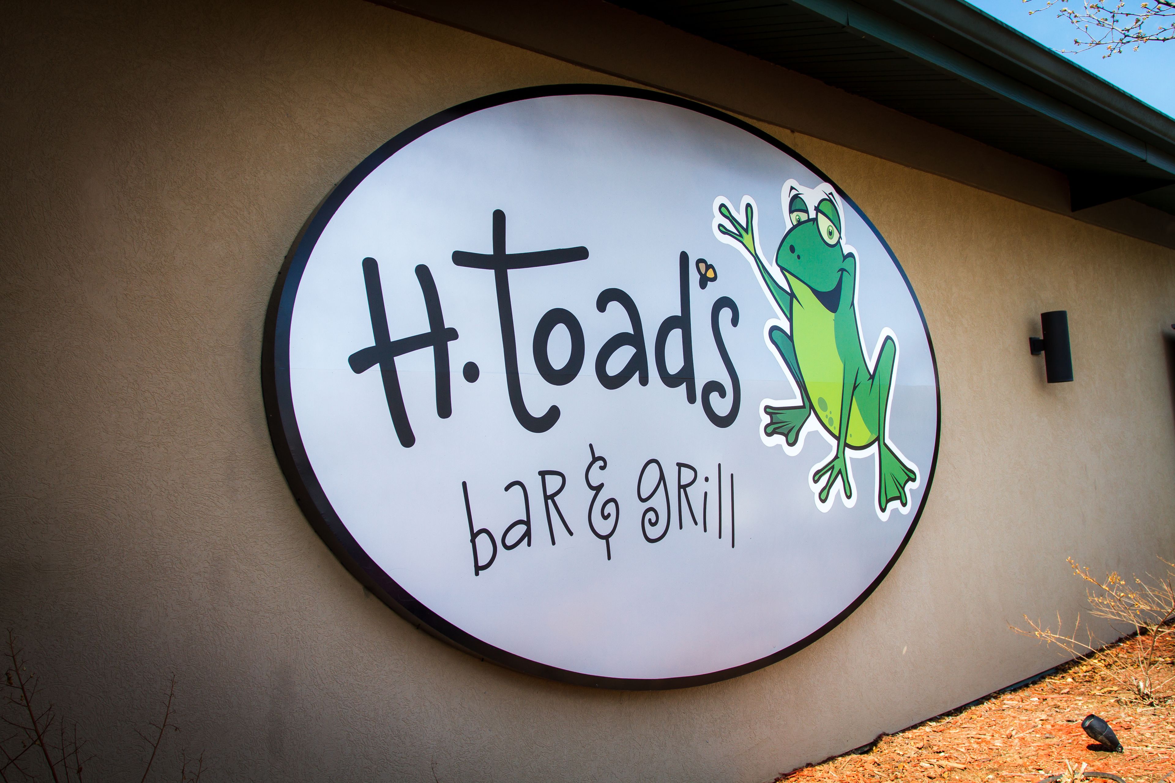 Un panneau circulaire pour le bar et restaurant H. Toads, avec une illustration d’une grenouille.