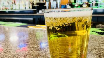A glass of beer on a bar counter with a blurred background of a bar and shelves of bottles.