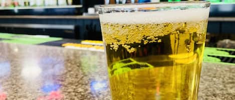 A glass of beer on a bar counter with a blurred background of a bar and shelves of bottles.