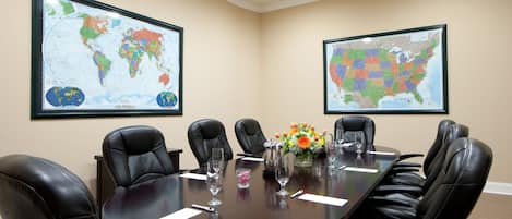 A conference room with a dark wooden table, black leather chairs, and two large world maps on the walls.