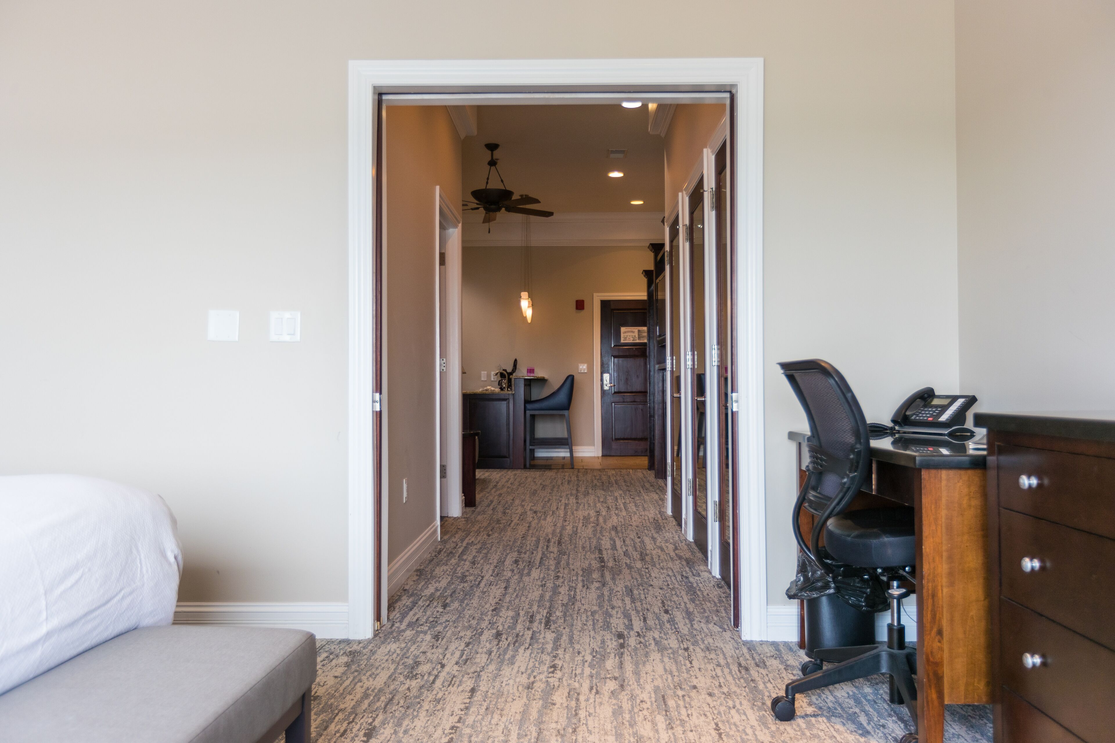 A hotel room with a bed, a desk with a chair, a phone, and a small kitchenette area.
