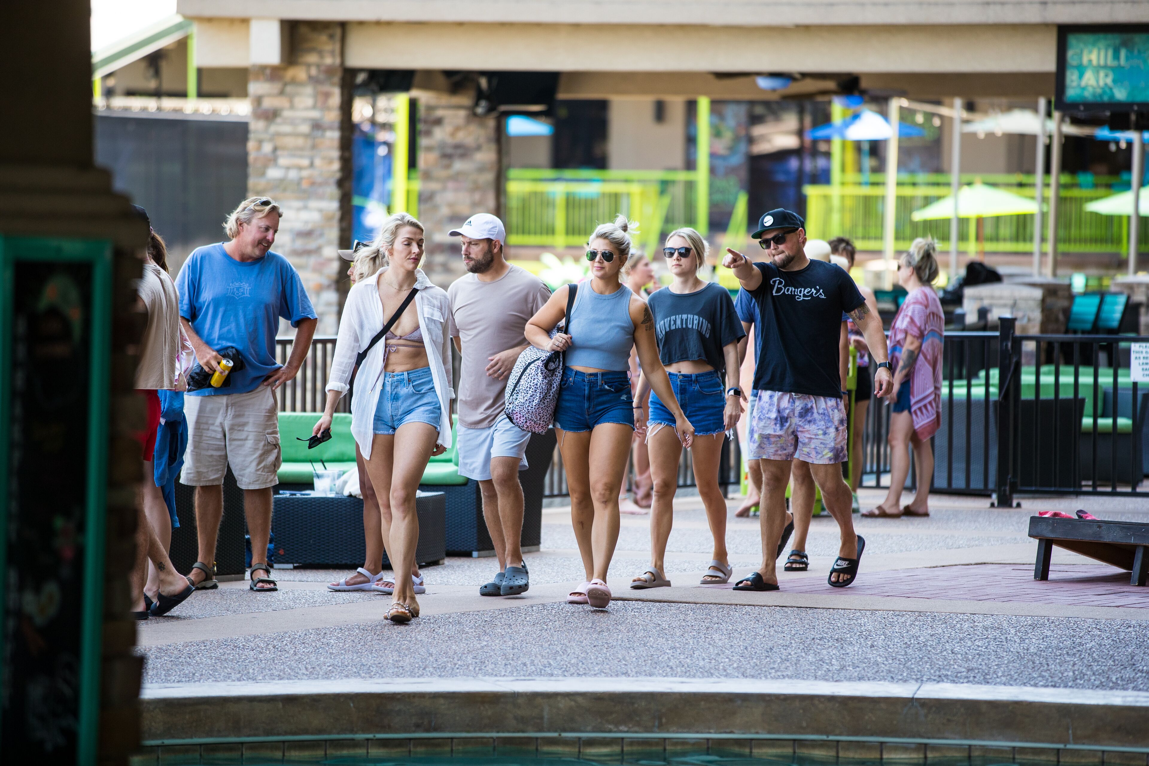 A group of people walking near a pool area with a sign for a 'Chill Bar' in the background.