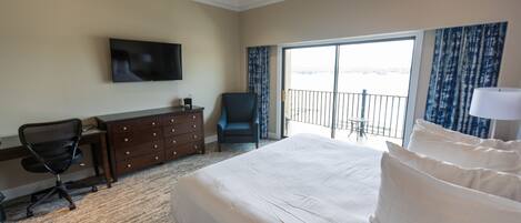 A hotel room with a bed, a desk, a chair, a dresser, a television, and a balcony with curtains.
