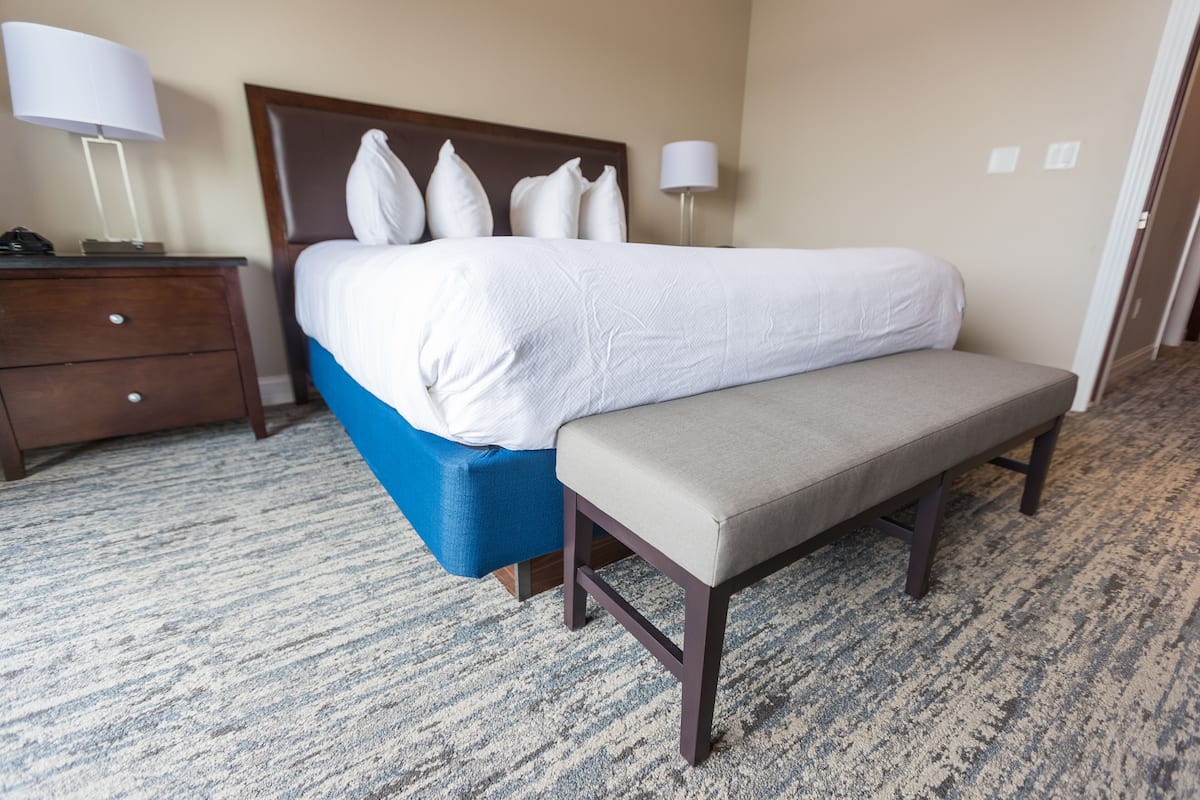 Ein Hotelzimmer mit Bett, Sitzbank, Nachttisch und Lampe.