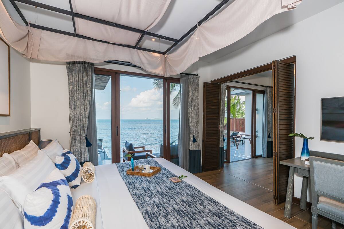 Un dormitorio con una cama grande, vistas al mar y un balcón con mesa y sillas.