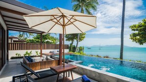 A poolside area with a wooden deck, lounge chairs, and a large umbrella. - NH Collection Samui Peace Resort (Koh Samui)