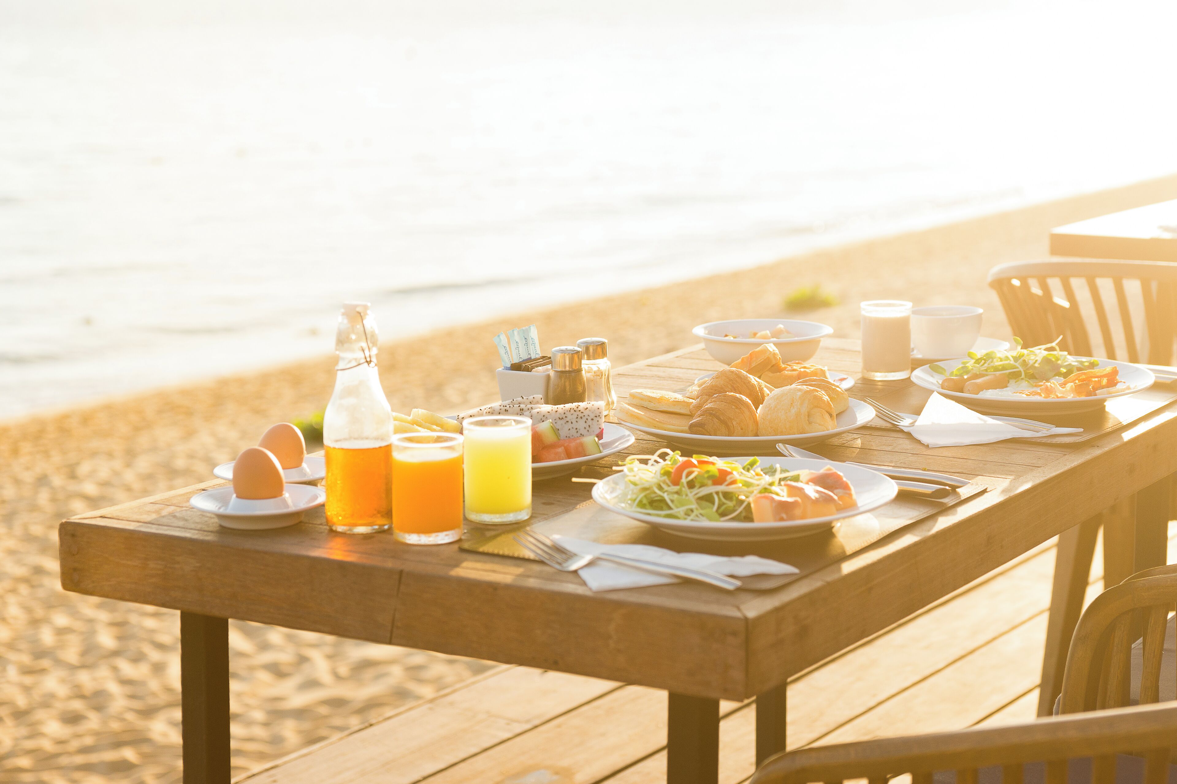 Una mesa de madera preparada con alimentos para el desayuno en la playa.