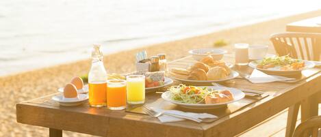 A wooden table set with breakfast items on a beach.