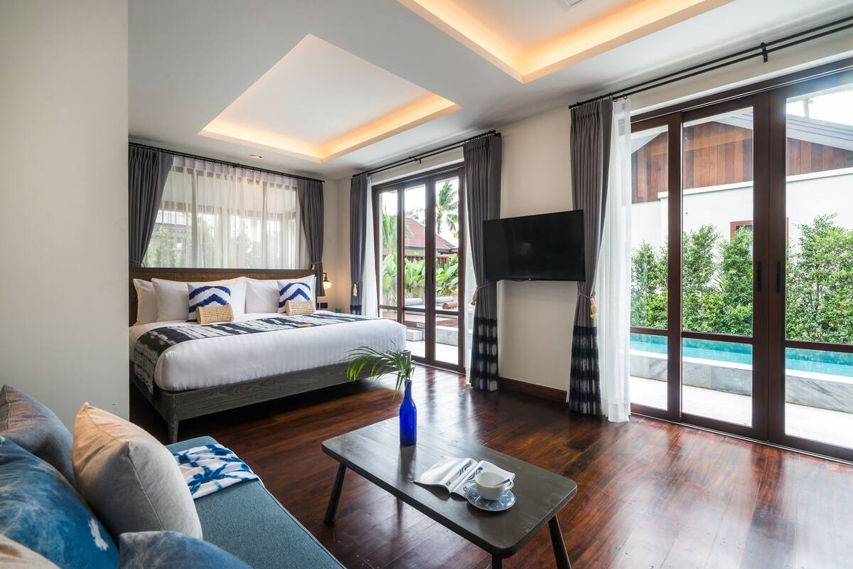 Una habitación de hotel moderna con una cama grande, un televisor de pantalla plana, una mesa de comedor y vistas a una piscina.