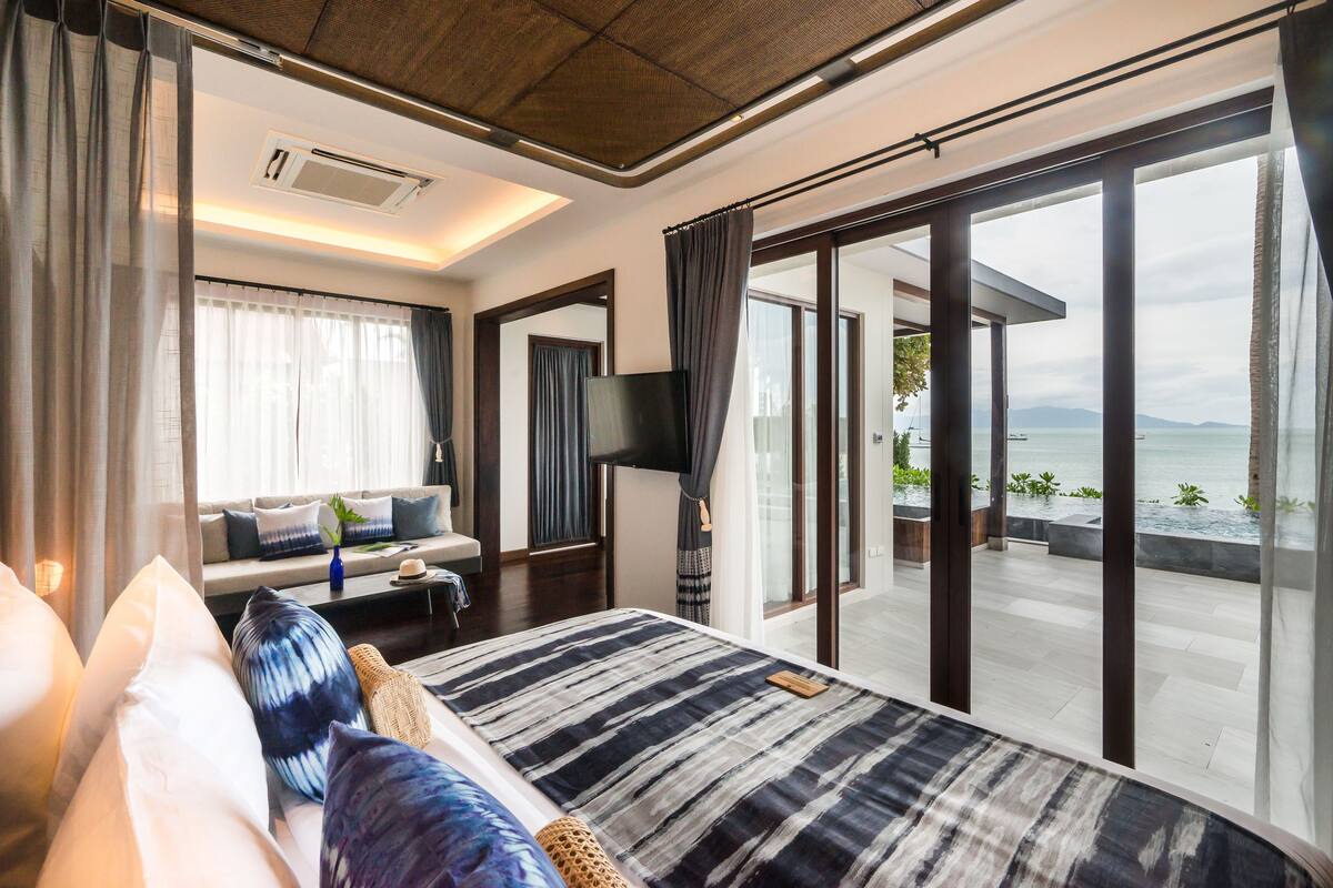 Una habitación de hotel moderna con una cama grande, un sofá, un televisor y un balcón con vistas al mar.
