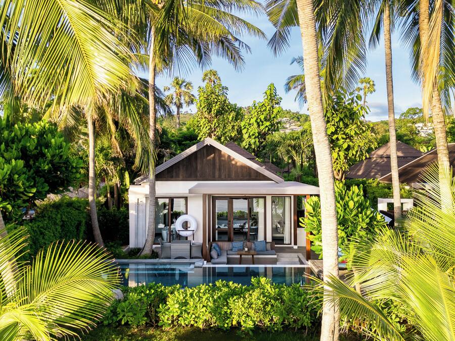 Una casa moderna con piscina, rodeada de exuberante vegetación y palmeras.