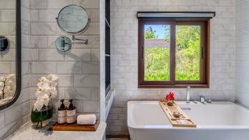 Un baño con bañera, ventana con vistas, espejo y estante con artículos de aseo.