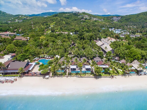 Un complejo turístico frente al mar con piscina, playa y abundante vegetación.