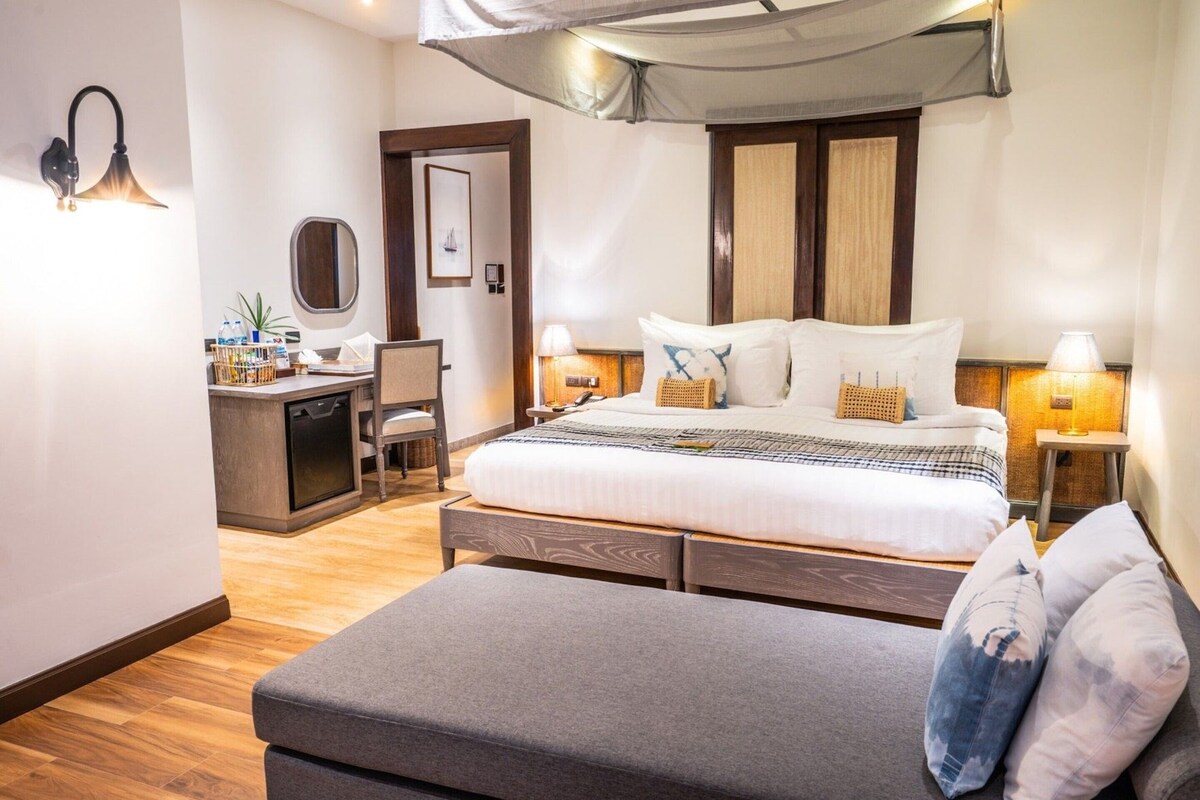 A hotel room with a bed, bedside tables, a desk, a chair, and a large window.