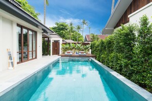 A swimming pool with a wooden deck and lounge chairs, surrounded by lush greenery and a clear blue sky. - NH Collection Samui Peace Resort (Koh Samui)