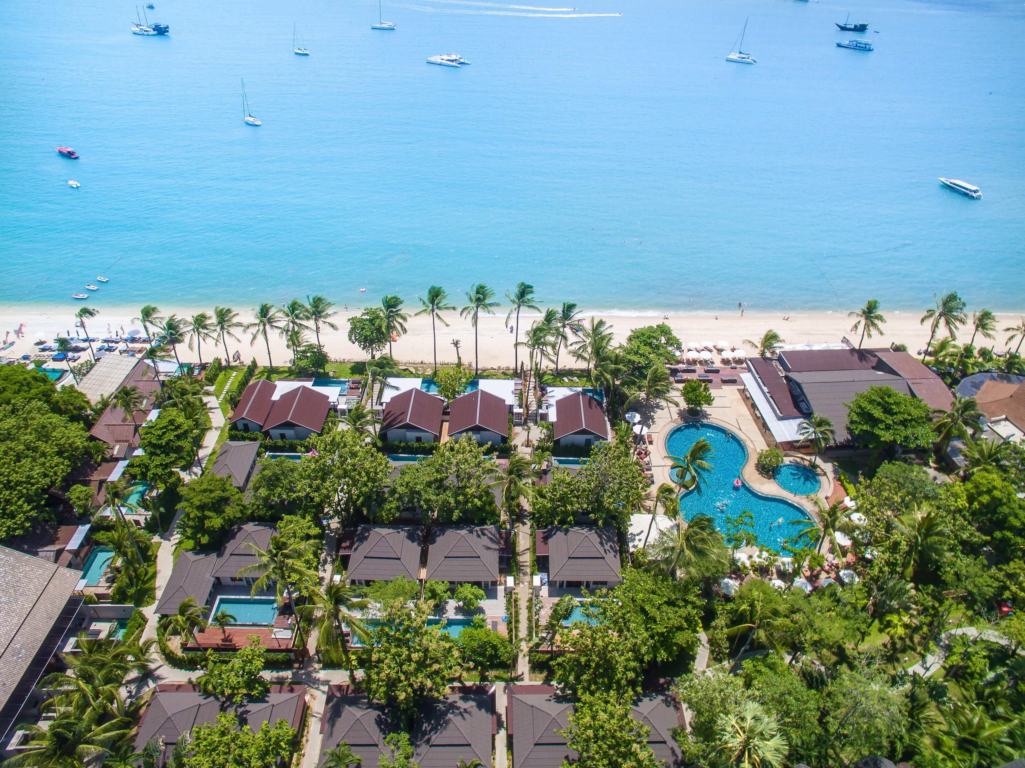 Un resort con varias piscinas, una playa y vistas al océano con barcos.