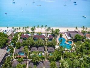 Un resort con varias piscinas, una playa y vistas al océano con barcos.