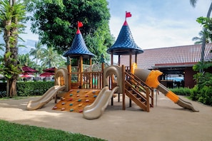 A playground with slides and climbing structures, surrounded by greenery and a building in the background. - NH Collection Samui Peace Resort (Koh Samui)
