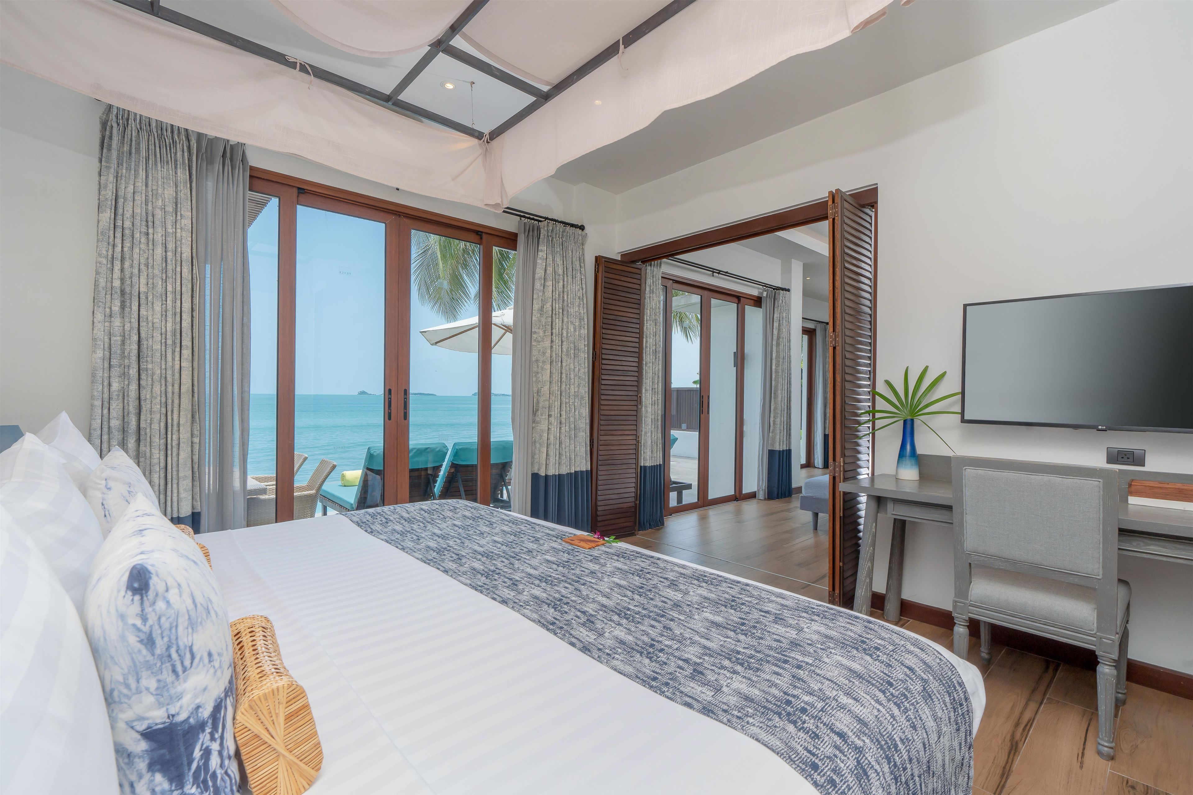 A hotel room with a bed, a desk, a television, and a view of the sea.