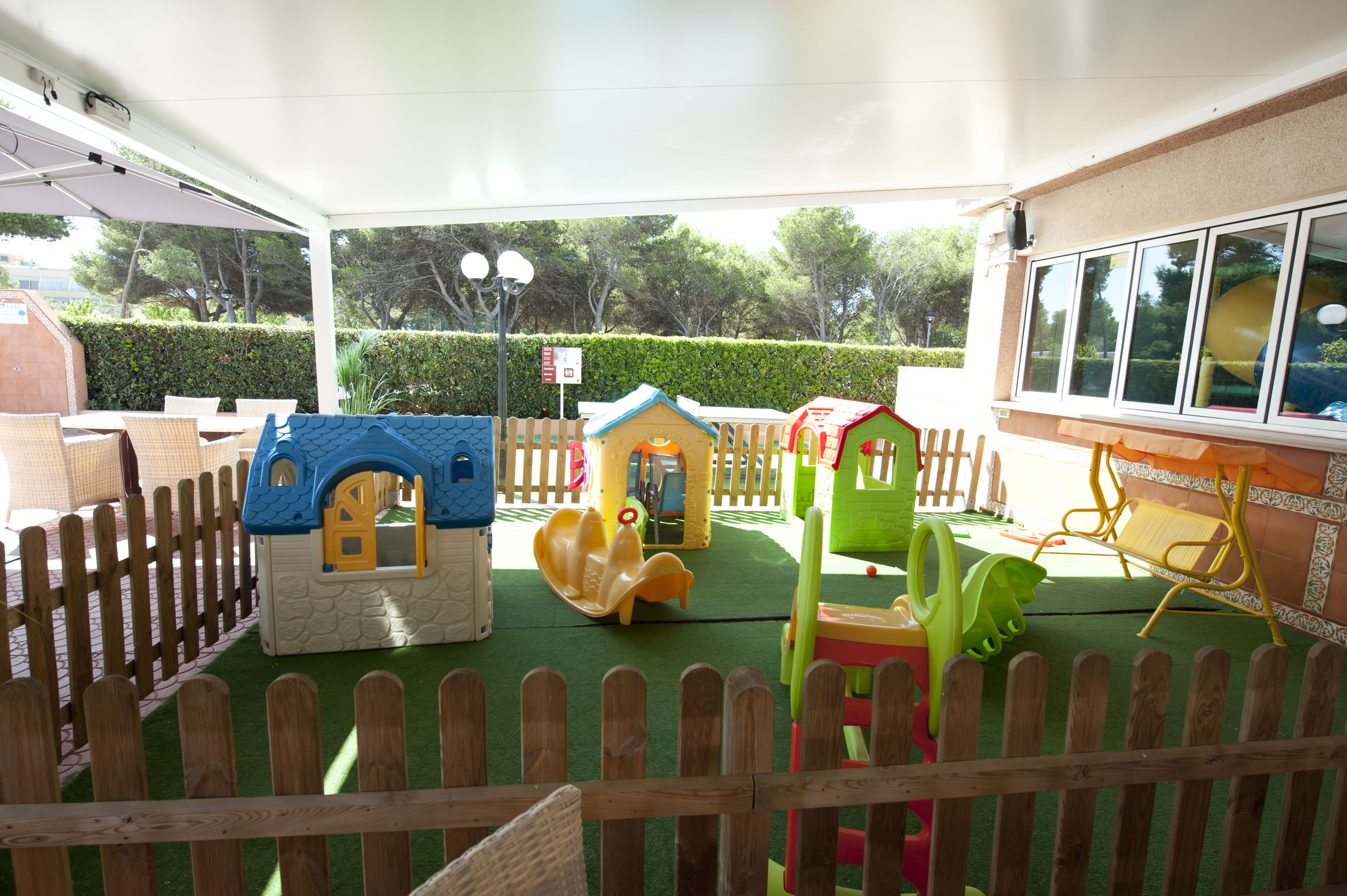 A covered play area with playhouses, slides, and a wooden fence.