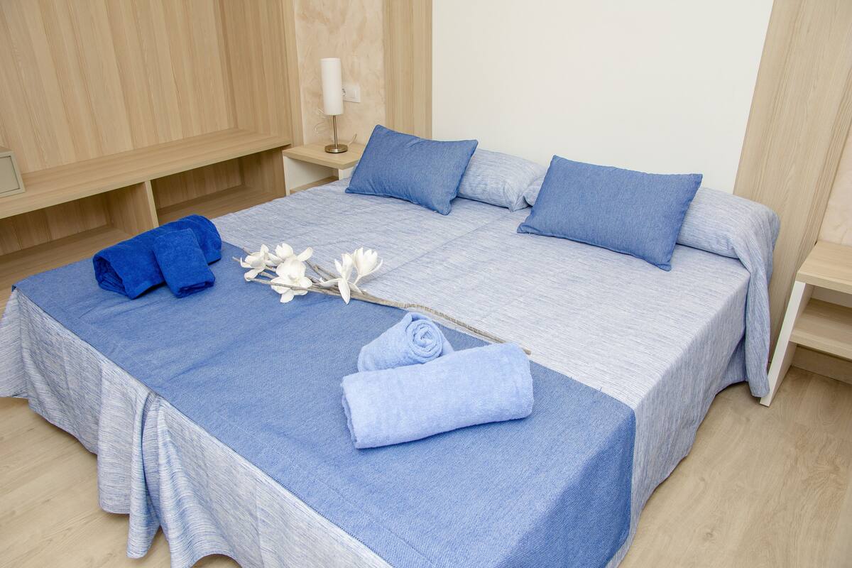 Un lit bien fait, avec une literie bleue, une table de chevet avec une lampe et une petite table en bois à côté du lit.