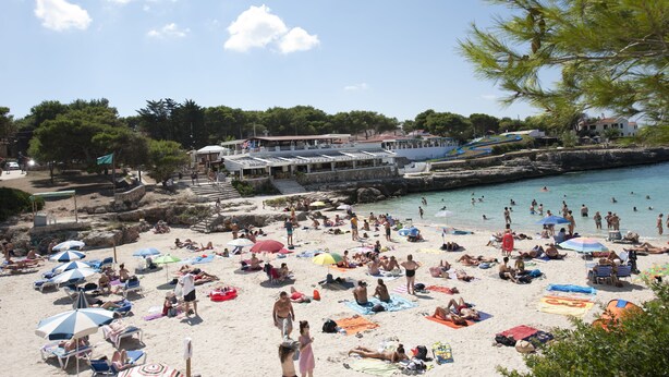 Ein überfüllter Strand mit vielen Sonnenschirmen und Menschen, die sich sonnen.